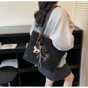 Detail of black tote bag with white horse pattern and 3D charm on model shoulder