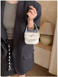 Detail of a white lace mini handbag featuring a decorative bow and heart texture