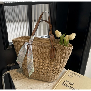 Detail of woven straw tote bag with leather handles and decorative floral silk scarf