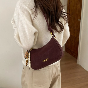Close-up of retro burgundy dumpling bag with knot strap and vintage beaded tassel detail