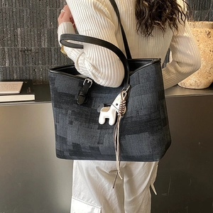 Detail of large tote bag with woven texture, leather strap, and white horse charm