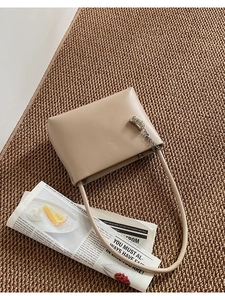 Detail of minimalist beige shoulder bag with silver metallic buckle on woven texture mat