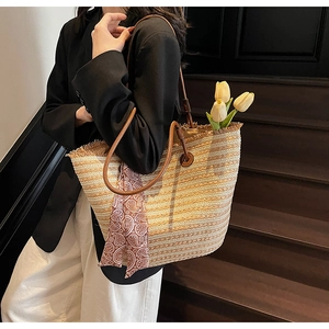Detail of striped woven straw tote bag with brown leather handles and decorative scarf