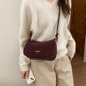 Close-up of wine red matte leather dumpling bag with gold lettering and knotted strap