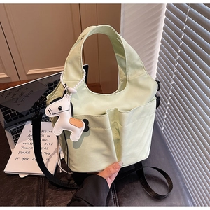 Dettaglio della borsa tote verde chiaro con doppie tasche frontali e ciondolo a cavallo