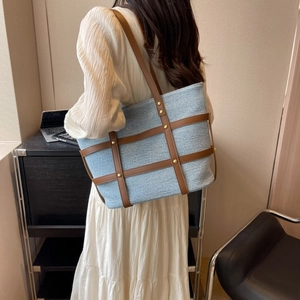 Detail of light blue denim tote bag featuring brown faux leather straps and gold rivets