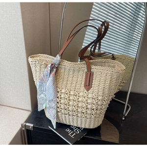 Detail of woven straw tote bag featuring intricate openwork patterns and a colorful silk scarf