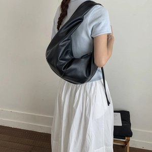 Close-up of black leather shoulder bag with natural pleats and wide strap on model