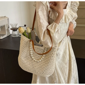 Detail of hand-woven straw tote bag with white pearl handle and brown leather shoulder strap