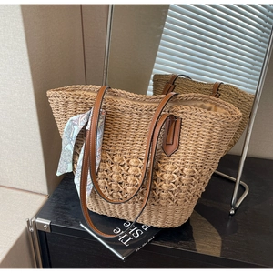 Detailed texture of hand-woven straw tote bag with brown leather handles and silk scarf