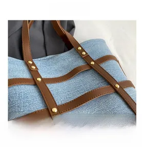 Close-up of blue denim tote bag with brown leather strips and gold metal rivets