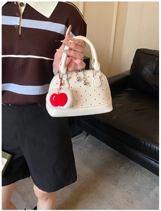 Detail of white shell handbag with red polka dots and apple plush charm accessory