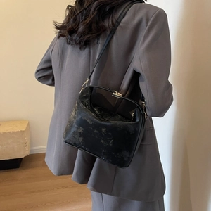 Detail of black textured PU leather bag with metallic clasp worn as a shoulder bag
