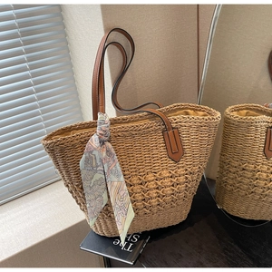 Detail of woven straw tote bag with brown leather handles and decorative silk scarf