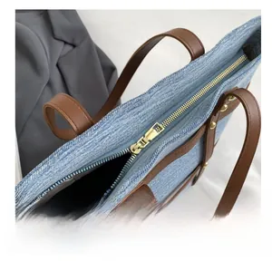 Detail view of smooth metal zipper and brown leather strap on denim patchwork tote bag
