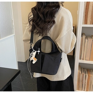 Dettaglio di una borsa tote nera a pieghe con tasche frontali e ciondolo a forma di cavallo
