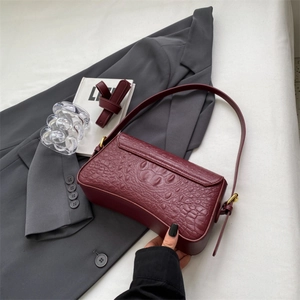 Dettaglio della borsa sottobraccio rosso scuro a trama coccodrillo su blazer grigio