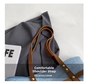 Detail view of denim tote bag showing brown leather straps with vintage gold metal rivets