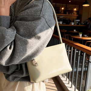Minimalist cream shoulder bag with silver crescent hardware shown in a sunset cafe setting