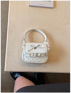 Detail of cream mini handbag with white lace trim, bow, and heart cutouts on top view