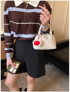 Chic white polka dot shell bag with red heart charm carried by a model in casual attire