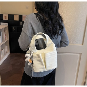 Modella che indossa una grande borsa tote in tela color crema con tracolla nera e ciondolo