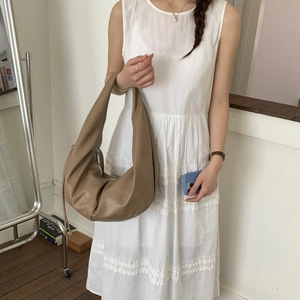 Brown leather crescent shoulder bag styled by a model in a minimalist white dress