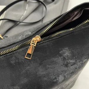 Detailed close-up of smooth gold metal zipper and distressed texture of black PU handbag
