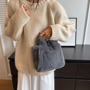 Détail d'un sac seau en fausse fourrure grise avec chaîne dorée sur un pull en tricot