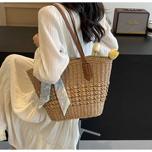 Detail of large straw tote bag with brown leather straps and colorful ribbon accent