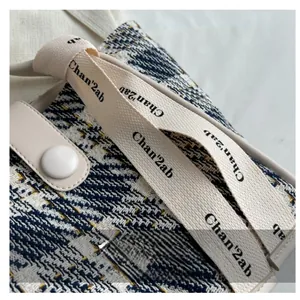 Close-up of blue and white tweed canvas tote bag with woven strap and leather snap closure
