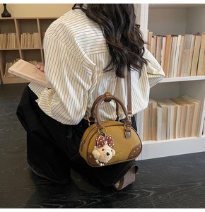 Close-up of ginger yellow Boston bag with gold rivets and cute bear charm in a retro setting