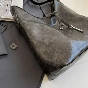 Detail of vintage grey leather tote showing waxy texture and drawstring metal ring buckle