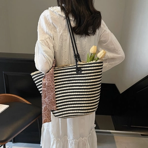 Large striped straw tote bag with black leather handles and silk scarf detail for beach