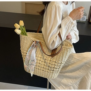 Close-up of woven straw tote bag with brown leather handles and a decorative printed scarf