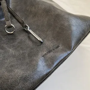 Close-up of distressed dark grey leather texture and silver buckle on a shoulder bag