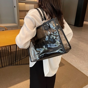 Close-up of a large transparent PVC tote bag with black PU leather straps and metal rivets