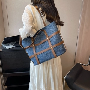 Detail of denim tote bag featuring brown leather lattice and gold rivets in office setting