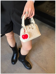 Close-up of cream polka dot shell bag with a red plush apple charm and silver zipper detail