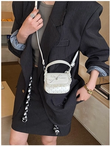 Close-up of a white mini lace crossbody bag with bow and heart charm on gray blazer
