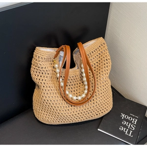 Detailed view of woven straw tote bag featuring brown leather straps and pearl chain accent