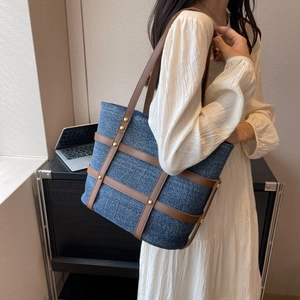 Detail of blue denim tote bag with brown leather trim and rivets carried by a model