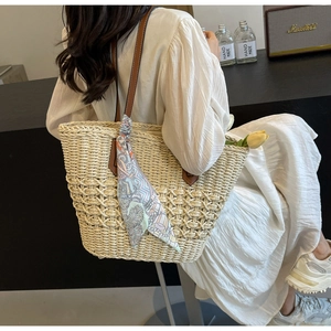 Close-up of woven straw tote bag featuring brown leather handles and a floral silk scarf detail