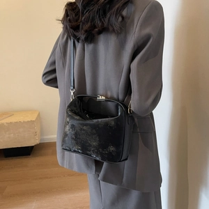 Detail of a black textured PU leather square bag worn with a grey suit for a modern look