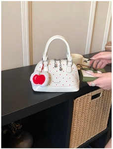 Detail view of white polka dot shell bag with red plush apple charm and silver hardware