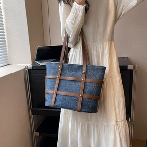 Detail view of denim patchwork tote with leather trim and gold studs on a model
