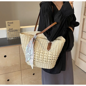 Detail of hand-woven straw tote with brown leather handles and a floral silk scarf