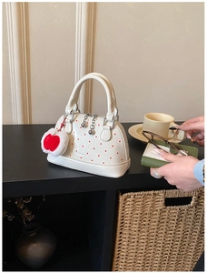 Close-up of cream shell bag with red polka dots and heart charm on a wooden shelf