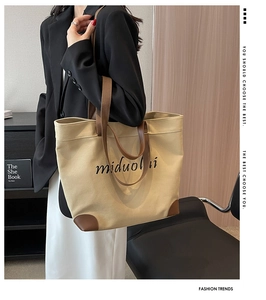Detail of minimalist beige canvas tote bag with brown leather handles and brand logo print