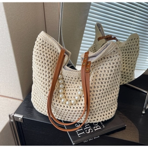 Detail of beige hollow woven straw tote bag with brown leather straps and pearl handle